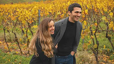 Two people standing in a vineyard talking to each other in sunshine.