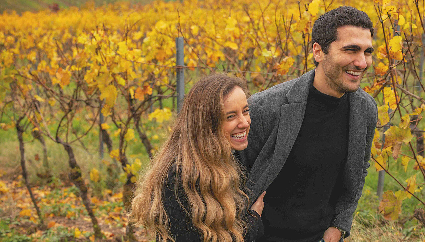 Zwei Personen stehen in einem Weinberg und unterhalten sich bei Sonnenschein.