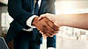 Nahaufnahme eines Händedrucks zwischen zwei Personen in formeller Kleidung.