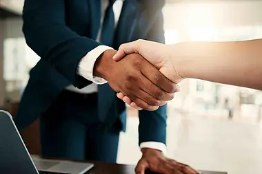 Nahaufnahme eines Händedrucks zwischen zwei Personen in formeller Kleidung.