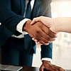 Nahaufnahme eines Händedrucks zwischen zwei Personen in formeller Kleidung.