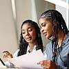 Two women sitting together, looking at a document.