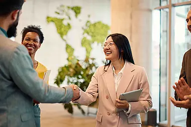 Drei Personen stehen zusammen und geben sich die Hand in einem Büro.