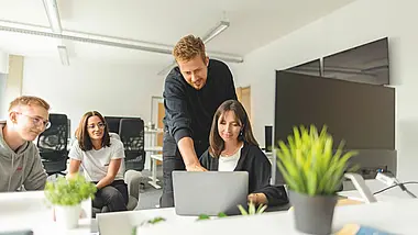 Gruppe von Menschen steht in einem modernen Büro mit Pflanzen und unterhält sich.