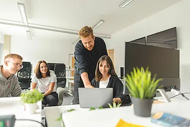 Gruppe von Menschen steht in einem modernen Büro mit Pflanzen und unterhält sich.