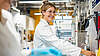 bild Woman in a white coat smiling in an industrial laboratory in front of machines.