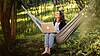 Woman sitting relaxed in a hammock outdoors and working on her laptop.