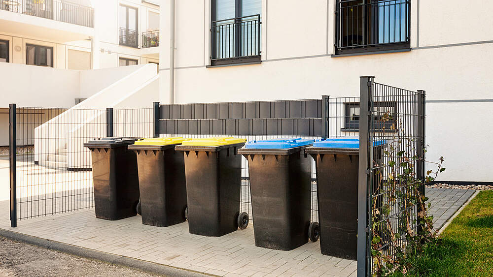 © AdobeStock / Irina Fischer Eine Reihe Mülleimer stehen ordentlich vor einem Neubau