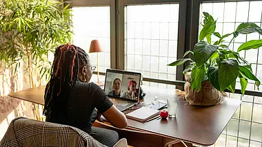 Woman seen from behind sitting at a round table in a bright room with plants.